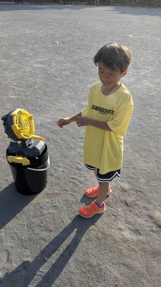 グラウンドでの練習中に涼しいドライミストを噴霧する黄色のTシャツを着た子供