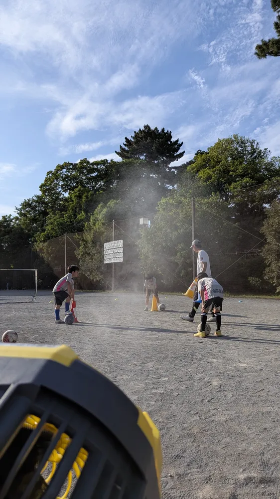 サッカー練習の合間にミストファンの周りに集まって笑顔を見せる子供たち